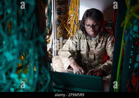 Hochwinkelporträt einer jungen afroamerikanischen Frau in Militäruniform Während der Verwendung des Computers im Serverraum Stockfoto