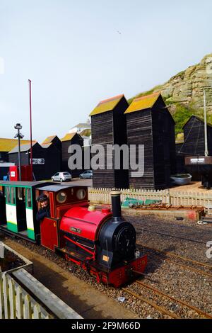 Frau, die mit der Dampflokomotive „Cornish Pixie“ an historischen Holzgeschäften auf der Hastings Miniature Railway, Hastings, East Sussex, England, vorbeifährt Stockfoto