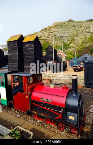Frau, die mit der Dampflokomotive „Cornish Pixie“ an historischen Holzgeschäften auf der Hastings Miniature Railway, Hastings, East Sussex, England, vorbeifährt Stockfoto