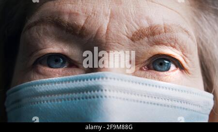 Nahaufnahme der blauen Augen einer alten grauhaarigen Frau mit Gesichtsmaske. Verletzliche ältere Person und Covid19. Hochwertige Fotos Stockfoto
