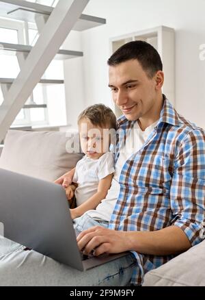 Glücklich junge Vater umarmt niedlichen kleinen Sohn Blick auf Laptop auf der Couch sitzen. Stockfoto