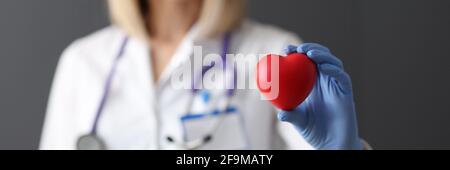 Doktor in Gummihandschuhen hält rotes Spielzeug Herz in seinem Nahaufnahme der Hände Stockfoto