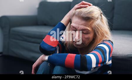 Ältere Frau, die unter Kopfschmerzen leidet, sitzt im Wohnzimmer auf dem Boden. Hochwertige Fotos Stockfoto