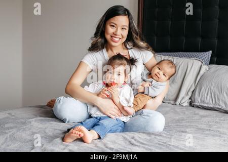 Asiatische chinesische glücklich Mutter sitzt auf dem Bett mit Tochter, neugeborenen Sohn. Stockfoto