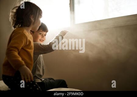 Ein Bruder und eine Schwester sitzen auf einem Bett und beobachten Strahlen Von Licht Stockfoto