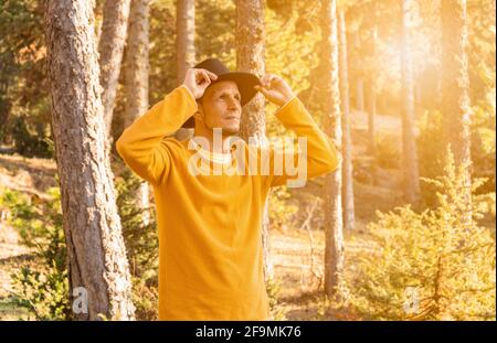Junge stilvolle Mann im Hut im Wald.Porträt kaukasischen Reisenden Cowboy in gelben Pullover im Wald bei Sonnenuntergang .schöne camping Landschaft mit Su Stockfoto