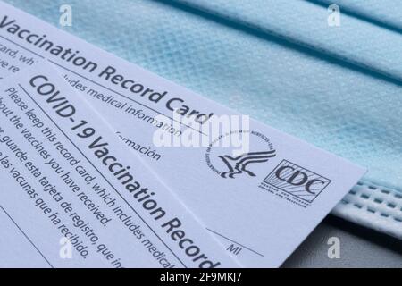 Nahaufnahme der von CDC (United States Centers for Disease Control and Prevention) ausgestellten Covid-19-Impfkarten auf einer blauen Einweg-Gesichtsmaske. Stockfoto