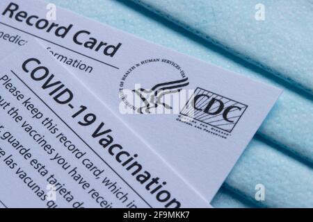 Nahaufnahme der von CDC (United States Centers for Disease Control and Prevention) ausgestellten Covid-19-Impfkarten auf einer blauen Einweg-Gesichtsmaske. Stockfoto