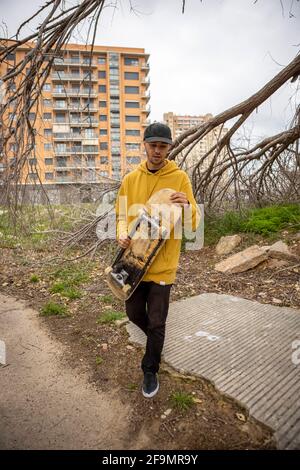 Junger Rüde in einem gelben Hoodie und einer Mütze mit einem Skateboard in seinen Händen Stockfoto