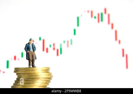 Miniatur kleine Menschen Spielzeug Fotografie. Die Menschen, die über dem Münzstapel stehen, haben kein Geld oder sind bankrott, die Aktienmarkt-Candle-Chart fiel herunter, isolieren Stockfoto