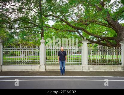 Das Asian Black T-Shirt steht nachmittags vor dem weißen Vintage-Zaun neben der Straße. Stockfoto