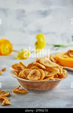 Bananenchips gesundes Essen, trockenes Obst und gesunde Gemüsechips, gesunder veganer Snack auf dem Hintergrund gelber Blumen. Stockfoto