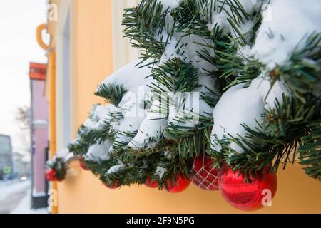Weihnachtsdekorationen im Freien am Fenster. Stilvolle Weihnachten verschneite Tannenzweige mit festlichen Kugeln auf einer Fensterbank auf der Straße eines festlichen Stockfoto