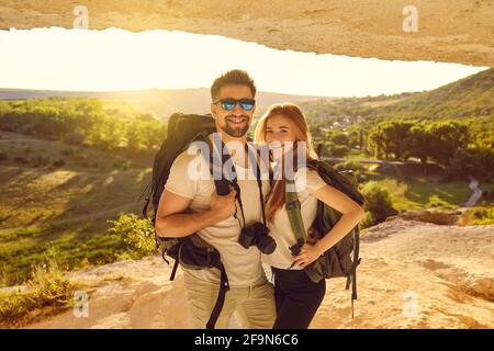 Glückliches junges Paar Wanderer, die bei Sonnenuntergang in der Berghöhle stehen. Touristen Bergsteigen im Sommerurlaub Stockfoto