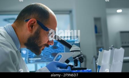 Man-Forscher, der Proben unter dem Mikroskop in einem modern ausgestatteten Labor betrachtet. Eldery Arzt, der mit verschiedenen Bakterien, Gewebe-und Bluttests, pharmazeutische Forschung für Antibiotika Stockfoto