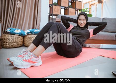 Eine Frau in einer Hijab-Sportkleidung lächelt beim Sit-Ups Trainiert ihre Bauchmuskeln Stockfoto