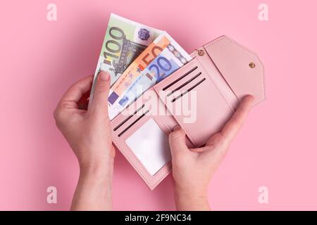 Hände halten Geldbörse. Geldbörse aus rosa Leder mit Euro-Geld in weiblichen Händen. Nahaufnahme der Hände einer Frau, die europäische Banknoten aus dem Geldbeutel nimmt und sich aufhält Stockfoto