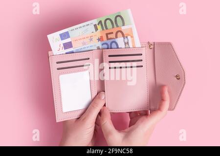 Hände halten Geldbörse. Geldbörse aus rosa Leder mit Euro-Geld in weiblichen Händen. Nahaufnahme der Hände einer Frau, die europäische Banknoten aus dem Geldbeutel nimmt und sich aufhält Stockfoto