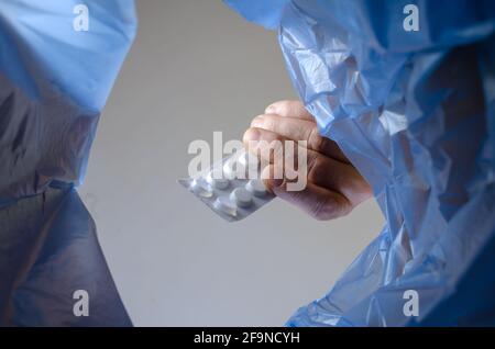 Die Hand wirft den Teller mit Pillen in den Müll. Ein Mann hält die unbrauchbaren abgelaufenen Medikamente über einem Abfalleimer in der Halle. Ansicht von unten. Stockfoto