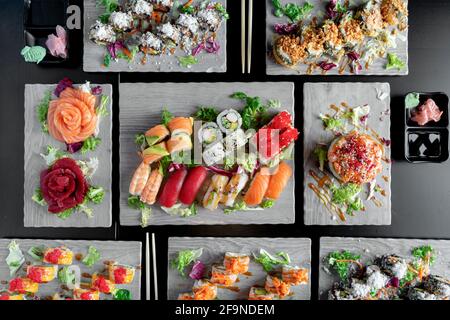 Draufsicht auf verschiedene japanische Gerichte auf dunklem Hintergrund. Sushi mit Thunfisch, Lachs, Agacate, Sashuimi und kalifornischem Brötchen. Stockfoto