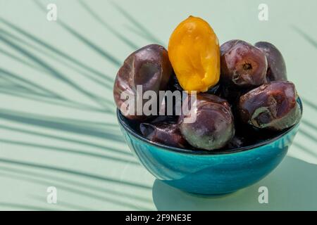 Religiöses moslemisches Fest und heiliger Monat des Ramadan, EID MUBARAK, Konzept: Nahaufnahme einer blauen Schale mit vielen getrockneten Datteln. Eine gelbe Dattfrucht. Handfläche Stockfoto