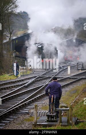 Historische Dampfeisenbahn oder Lok, die Rauchwolken auf der historischen Eisenbahn aufblähen (Mann in Overalls nach Punkten) - Oxenhope Station Sidings, Yorkshire, England Stockfoto