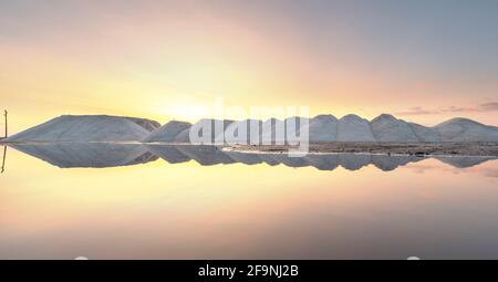 Meersalzproduktion in der Nähe des Salzsees Pomorie, Bulgarien. Salzberge in der Fabrik bei Sonnenuntergang mit Spiegelung im Wasser. Stockfoto
