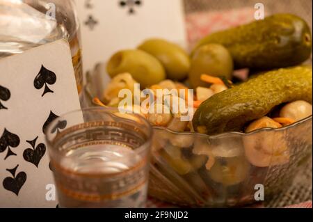 Spielkarten, ein Glas Wodka, ein Dekanter Wodka und eine Glasschale mit Gurken und Pilzen auf dem Tisch. Nahaufnahme, selektiver Fokus. Stockfoto