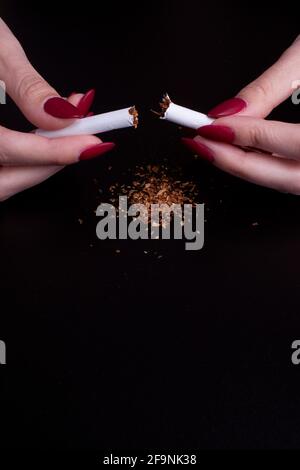 Rauchen von Zigaretten stoppen Konzept. Mädchen hält gebrochene Zigarette in den Händen auf schwarzem Hintergrund. Stockfoto