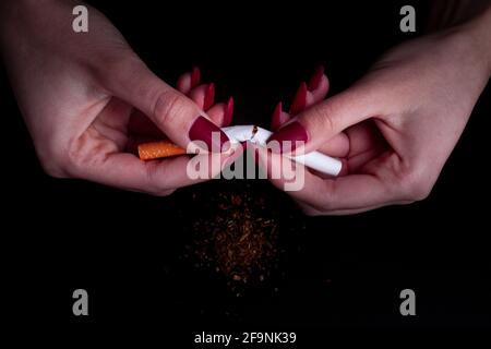 Rauchen von Zigaretten stoppen Konzept. Mädchen hält gebrochene Zigarette in den Händen auf schwarzem Hintergrund. Stockfoto