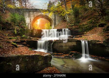 Herbstwasserfälle in der Nähe von Sitovo, Plovdiv, Bulgarien. Wunderschöne Wasserkaskaden mit gefallenen gelben Blättern unter der Brücke. Sitovski Wasserfall Stockfoto