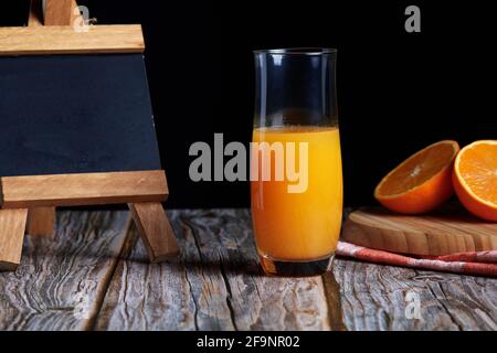 Kanne frisch gepressten frischen Orangensaft mit frischen Früchten auf Holztisch. Kleine Tafel für Kopierraum und schwarzen Hintergrund Stockfoto