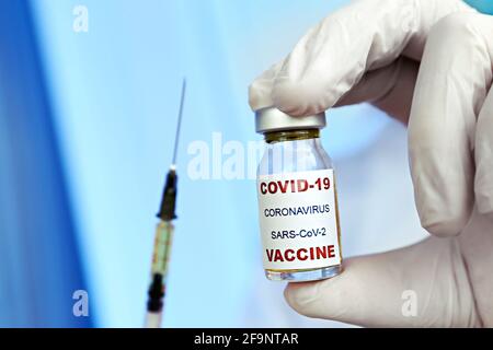Makroaufnahme der Hände eines Arztes in blauen Latexhandschuhen mit dem neuen Covid-19-Impfstofffläschchen und der mit Medikamenten gefüllten Oberfläche. Nahaufnahme, Kopierbereich, Backgr Stockfoto