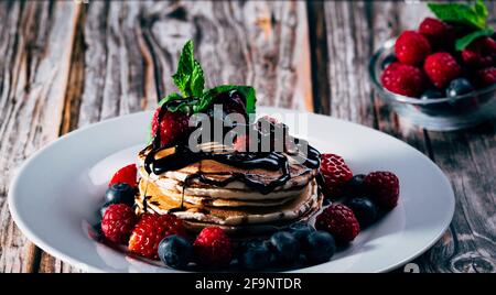 Gesundes Frühstück, hausgemachte klassische amerikanische Pfannkuchen mit Erdbeeren, Himbeeren, frischen Blaubeeren und Schokoladensirup. Nahaufnahme Stockfoto