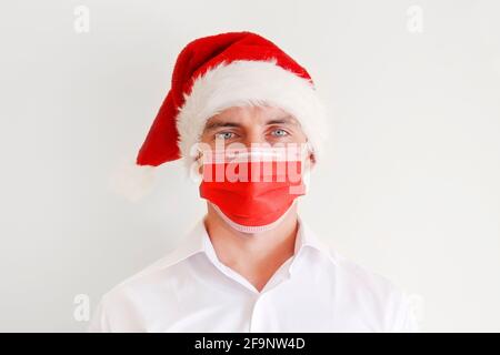 Nahaufnahme Porträt des Mannes mit leuchtend blauen Augen tragen weißes Hemd, Weihnachtsmann Hut und rote Gesichtsmaske isoliert auf weißem Hintergrund. Weihnachtsfest Stockfoto