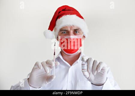 Coronavirus-Impfstoff als weihnachtsgeschenk Konzept. Porträt eines Arztes mit Weihnachtsmann-Hut, roter Gesichtsmaske und Latexhandschuhen, die den neuen Covid-19 vorführen Stockfoto