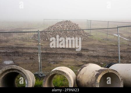 Kanalrohre und ein Stapel Pflaster hinter einem Zaun auf der Baustelle im Nebel, Niederlande Stockfoto