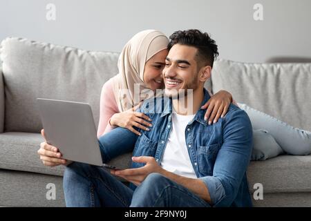 Liebevoller Mann aus dem Nahen Osten zeigt seiner Frau etwas auf dem Laptop Stockfoto
