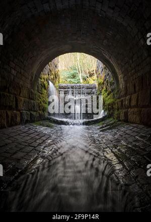 Gruselig dunkel unheimlich alten Kanalisation Backstein Tunnel gruselig Wasser Fluss läuft durch fließendes Licht am Ende. Wasserfälle in alten keulen lange Belichtung verschwommen Stockfoto