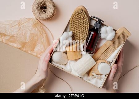 Beauty-Abonnement Vorbereitung von Box. Weibliche Hände halten Geschenkbox mit natürlichen Hautpflegeprodukten, Körperbürste, Shampoo, Seife, Feuchtigkeitscreme. Stockfoto