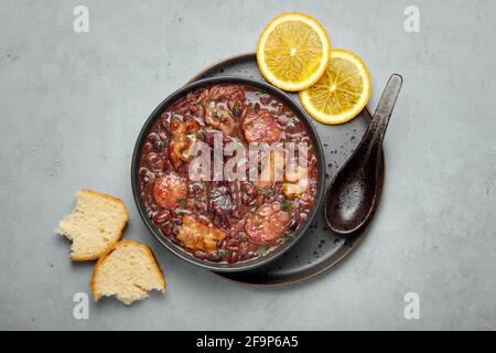 Feijoada in schwarzer Schale grau Beton Tischplatte. Brasilianische und portugiesische Küche traditionelle Bohnen-Fleischeintopf Stockfoto