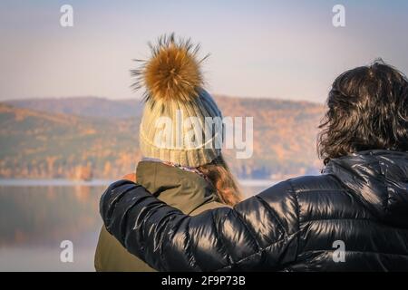 Das junge Paar blickt in die Ferne zum gegenüberliegenden Ufer Des Sees im Herbstwald Stockfoto