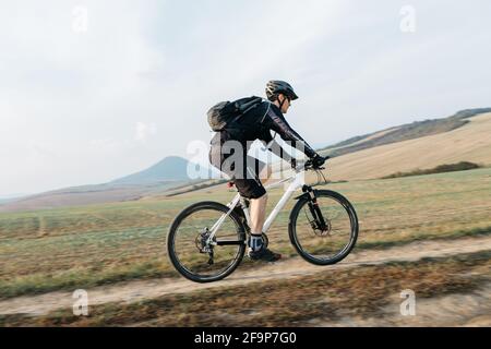 Mann Mountainbiken auf Feldweg. Radfahrer fahren Fahrrad entlang Schotterstraße an klaren sonnigen Tag. Stockfoto