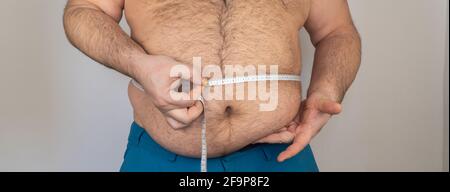 Fat Mann misst die Größe des Bauches mit einem Zentimeter Maßband. Person ist übergewichtig, er ist übergewichtig. Stockfoto