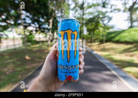 Linke Hand hält einen Mango Loco Monster Energy Drink in der Mitte des Pflasters. Stockfoto