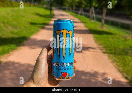 Die linke Hand hält Monster Energy Drink im Freien. Trinke ein Monster, während du auf dem Trail läufst. Energie für schnelleren und längeren Betrieb bereitstellen. Stockfoto