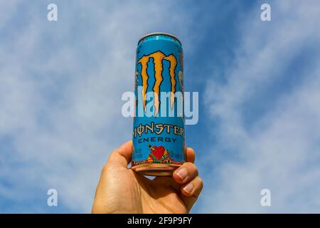 Eine Hand hält Monster Energy Drink Dose gegen den wolkenblauen Himmel. Stockfoto