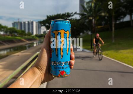 Die linke Hand hält eine Dose Monster Energy Drink, um deine Energie zum Radfahren zu tanken. Stockfoto