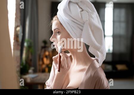 Junge Frau, die Make-up auf ihr Gesicht mit Make-up Pinsel Vor dem Spiegel Stockfoto