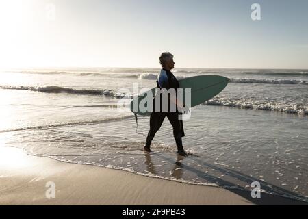 Senior african american Frau trägt Surfbrett zu Fuß am Strand. Reise Urlaub Ruhestand Lifestyle-Konzept Stockfoto